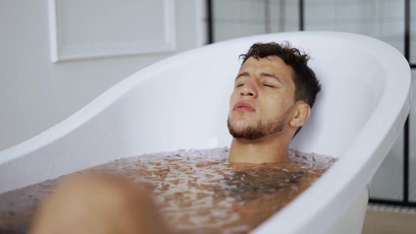Man sits with closed eyes in the bath with ice cubes for recovery Royalty-Free Stock Footage #1078388012
