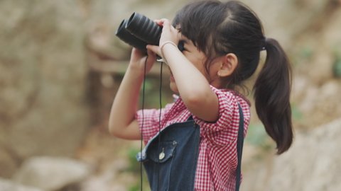 Asian Child Looking in Binocular on Meadow, Happy Tourist Little Girl Relaxing on Green Grass in Trip, Sightseeing, Landscape Seen in Spyglass, Children in Camping Learning about Nature