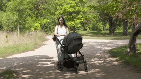 Mother with baby stroller on a walk outdoors, mom pushing baby carriage along park alley on a sunny summer day. High quality 4k footage