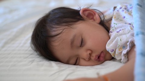 mixed cute baby girl sleeping on bed, lies prone on her tummy, smilies happy in a dream