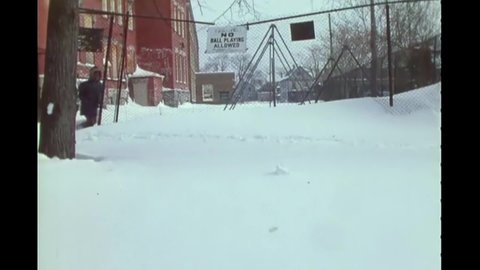 CIRCA 1977 - A child walks through heavy snowfall outside their school in Buffalo, New York. Trucks drive through a neighborhood blanketed in snow.