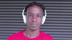 Portrait of young african american man listening to music with headphones while looking and smiling at camera outdoors - Millennial generation and multiracial people concept