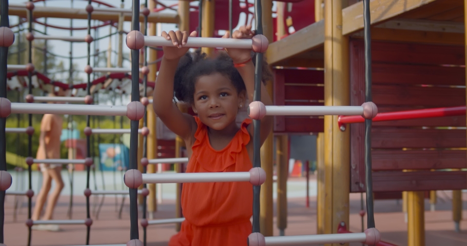African kid having fun with climbing net outdoors. Happy little afro-american girl playing on playground in summer park Royalty-Free Stock Footage #1078399808