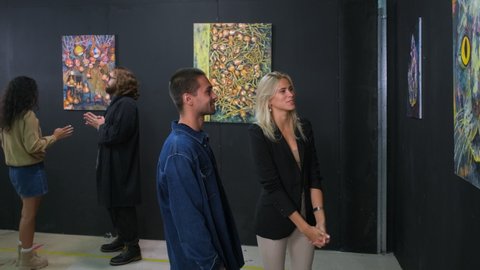 young people are enjoying modern art in gallery with abstract pictures of trendy artist, visitors on hall of museum of fine art, men and women are discussing painting