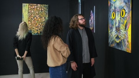 group of art lovers are visiting modern museum, viewing pictures, man and woman are communicating and discussing work of trendy artist