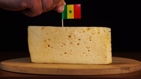 Man's hand put small in size toothpick with senegalese flag on cheese.
