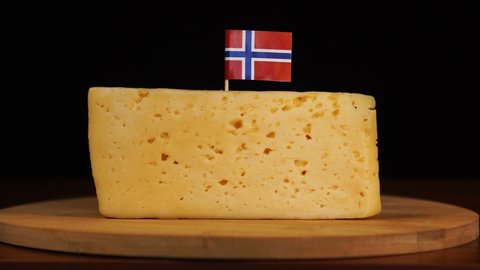 Man's hand put small in size toothpick with norwegian flag on cheese.