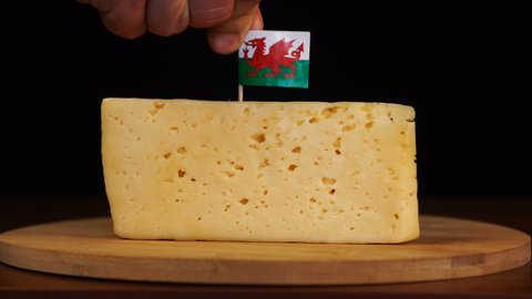 Man's hand put small in size toothpick with welsh flag on cheese.