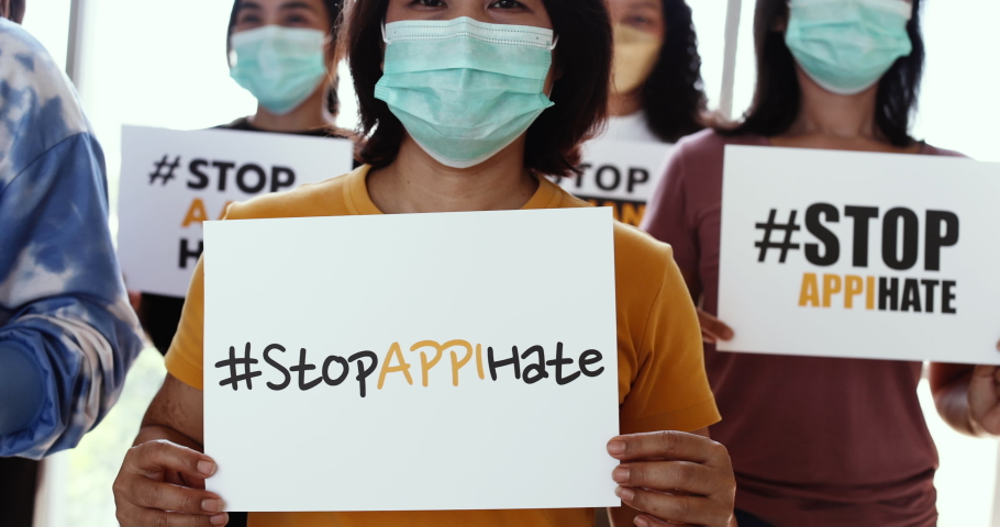 Group of multi races Asian women wearing protective hygiene face masks shake banners during participants in Asian American Pacific Islanders rally marching protest to stop hate on AAPI citizen. Royalty-Free Stock Footage #1078406804