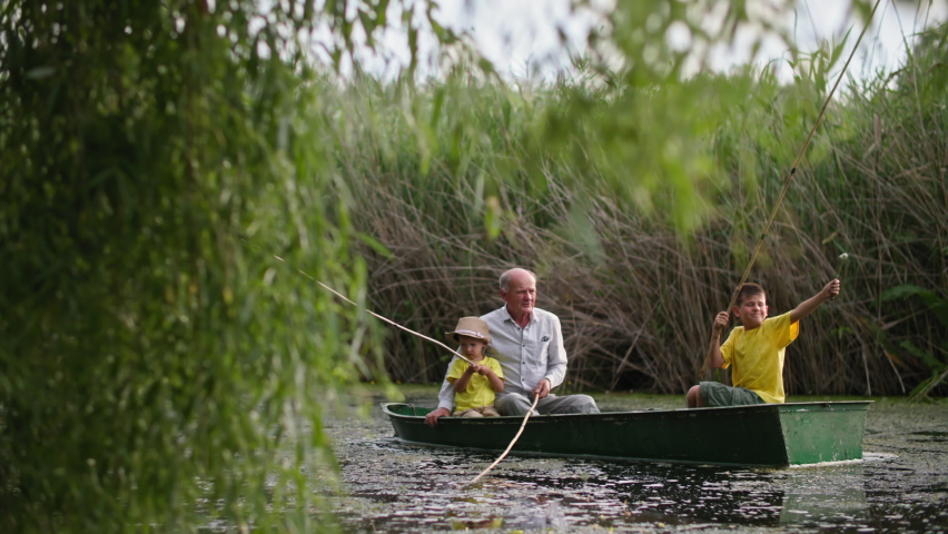 granddad and grandsons on boat catch fish from river on background of green reeds, family rest together outdoors