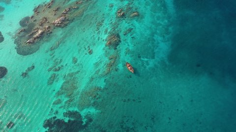 View from above, stunning aerial view of a wooden boat anchored to some rocks bathed by a crystal clear, turquoise water. Giardinelli island, La Maddalena Archipelago, Sardinia, Italy.