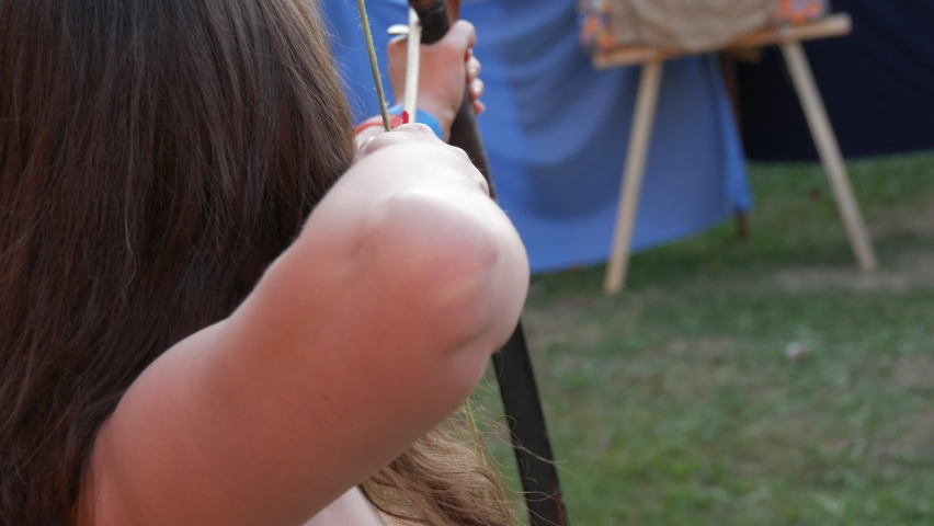 Woman archer with long hair shoots from a bow with arrows at a target, view from the back
