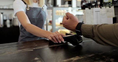Close up customer for takeaway coffee paying with an NFC contactless smartwatch with a card machine. Paying in a coffee shop by a smartwatch. Technology.