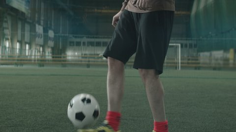 Tilt up shot of Caucasian male athlete in sportswear juggling soccer ball on indoor sports field