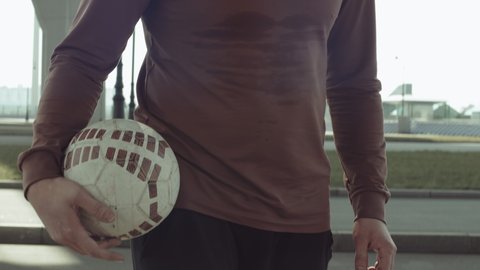 Wide shot of male football player in sportswear walking on urban street and juggling soccer ball