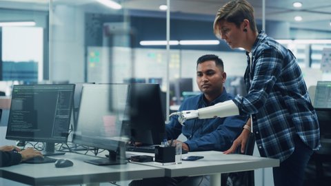 Teamwork In Diverse Inclusive Office: Project Manager with Disability points Prosthetic Arm at Screen Talks with Indian Specialist Working on Computer. Professional Creative Software Engineers