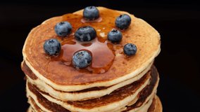 Pancakes with blueberry and maple syrup on black background. Pancake Maple syrup pouring onto stack of pancakes. 4K UHD video 