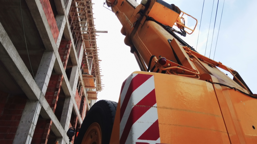 Yellow automobile crane with risen telescopic boom outdoors over blue sky, construction site
