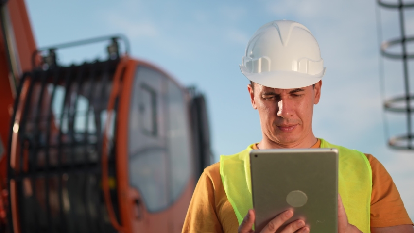 worker in hard a hat with digital tablet near excavator. construction site driver with digital tablet. industry construction concept. worker in hard hat near excavator truck in business uniform. Royalty-Free Stock Footage #1078436954