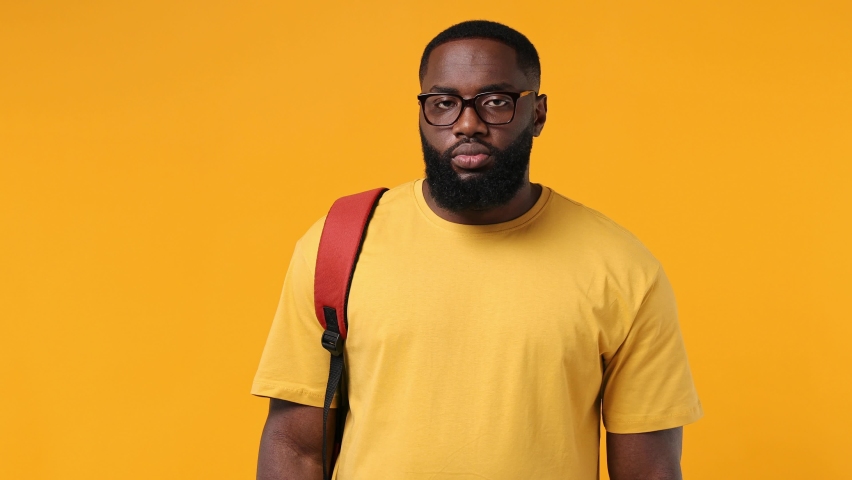 Excited young african american man 20s wears orange t-shirt backpack glasses hold book with blank screen workspace area show thumb up like gesture isolated on plain yellow background studio portrait Royalty-Free Stock Footage #1078443800