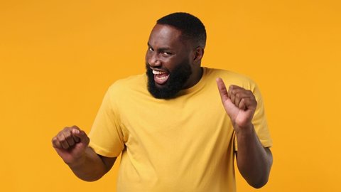 Excited jubilant overjoyed happy young bearded african american man 20s wears orange t-shirt doing winner gesture celebrate clenching fists say yes isolated on plain yellow background studio portrait