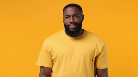 Secret fun young bearded african american man 20s years old wears orange t-shirt look aside away say hush be quiet with finger on lips shhh gesture isolated on plain yellow background studio portrait