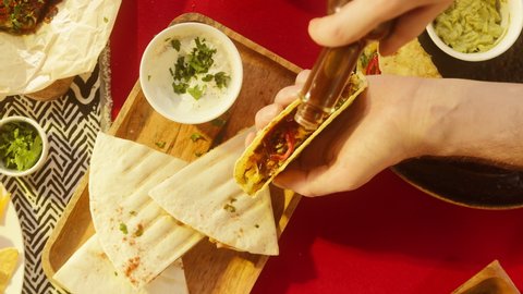 Traditional Mexican food, tex mex cuisine. Cooked quesadilla on wooden tray, pouring sauce on tacos served with meat and vegetables, tomato soup with cilantro, guacamole top view.