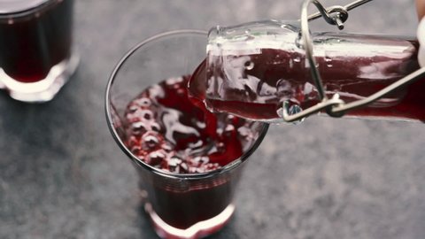 Pouring black elder syrup from a bottle into a glass, slow motion
