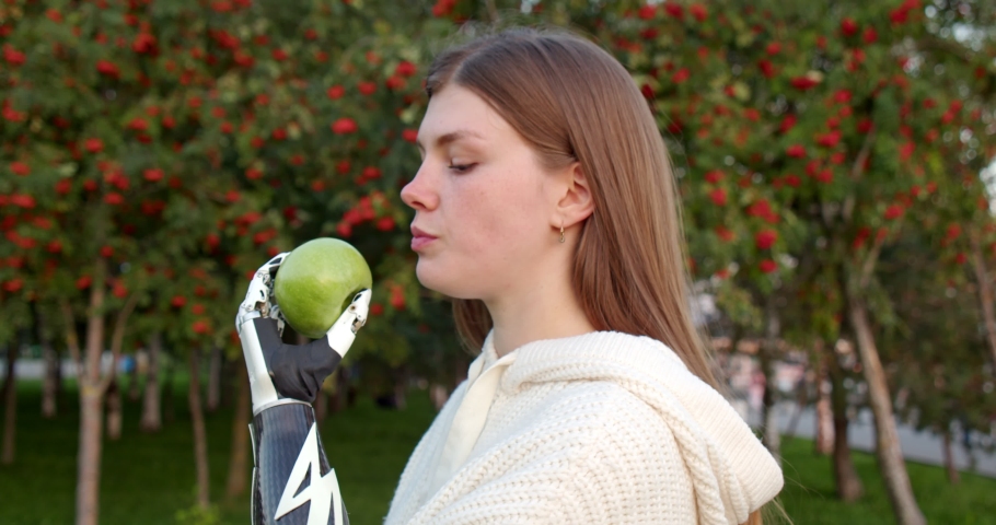 Portrait of a girl who eats an apple with a bionic hand. the use of a prosthesis and a robotic hand in everyday life. modern technologies in orthopedics | Shutterstock HD Video #1078453847
