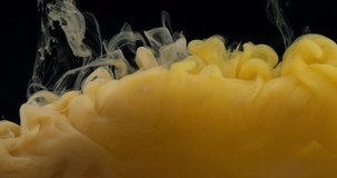 Yellow paint dissolves in water on a black background, abstract dark paint in water in an aquarium, slow motion video, 4K.