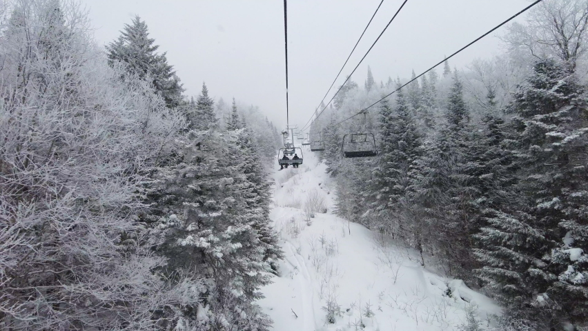 Ski lift in idyllic winter landscape with snow and trees. Beautiful snowing weather on extremely cold day at ski resort with classic ski chairlift. Unrecognizable people in ski lift Royalty-Free Stock Footage #1078461974