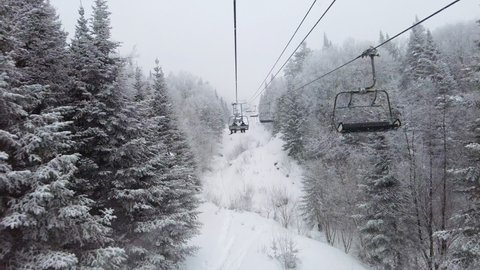 Ski lift in idyllic winter landscape with snow and trees. Beautiful snowing weather on extremely cold day at ski resort with classic ski chairlift. Unrecognizable people in ski lift