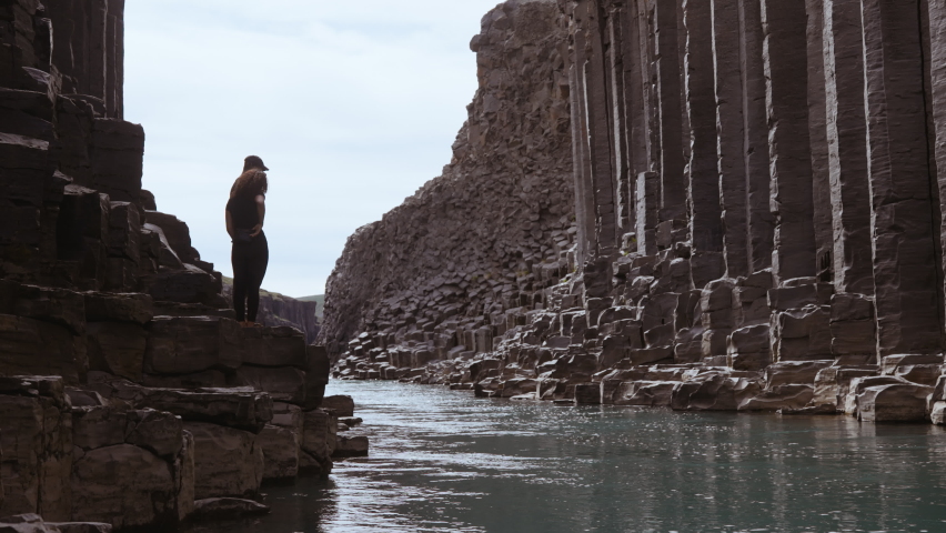 Steady shot of a man and woman standing on the rock formations by the side of the river in Studlagil Canyon in Iceland