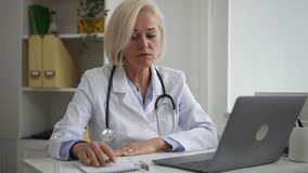 Doctor distance appointment internet resources. Mature female family physician with stethoscope gives recommendations to patient at videochat in clinic