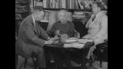 1940s: Albert Einstein, Leo Szilard and man are seated around table, man reads aloud from letter on table.