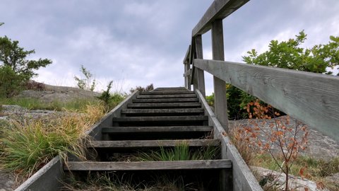 A wooden staircase nearby the ocean at the Swedish West coast. Early autumn in the Swedish nature. Cloudy grey sky. Stairway to heaven. 