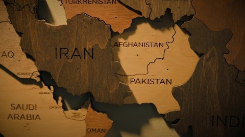 Wooden map with Afghanistan country and other countries borders. A man sticks red nail in Afghanistan country on wooden map. War conflict concept