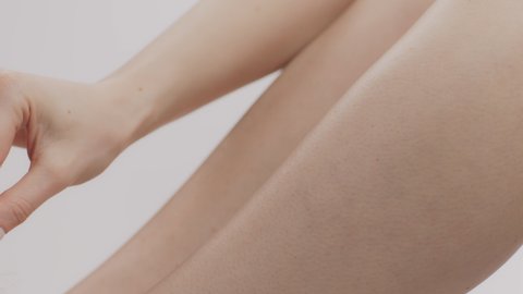 Best effective depilation cream. Close up shot of unrecognizable lady stroking her smooth legs with white feather, enjoying gentle skin, slow motion