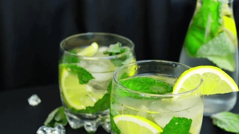 Slow motion Ice cube fall splash drops. Mojito refreshing cocktail, alcohol drink. Lemonade with lemon and mint leaves on dark background. Summer refreshing detox drinks. Clean eating, healthy