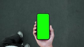 Young Man Walking and Use Green Screen Chroma Key Phone Point of View. Caucasian Person Hold in Hand Smartphone Mock-up and Watching Video Call, Copy Space Browsing. Go in Urban Mobile Phone Close-up