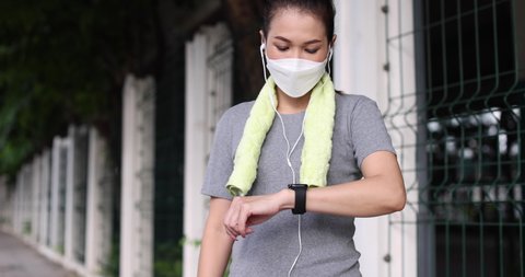 Sporty woman runner wearing protective mask on face and sports clothes touching and setting function on smartwatch mobile app before start running session for workout during coronavirus outbreak.