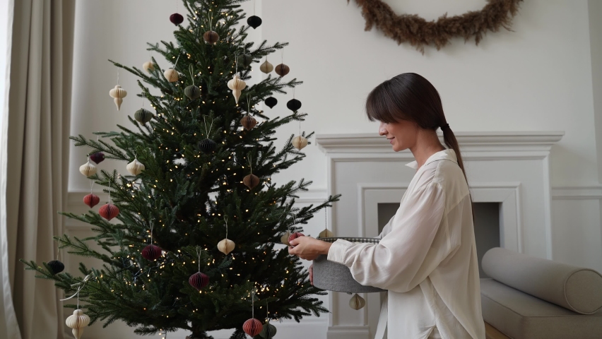 А girl dresses up a Christmas tree with toys. Modern, minimalistic Christmas decoration.