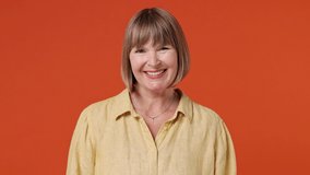 Smiling charming mature elderly senior elegant lady woman 55 years old wears yellow shirt looking camera wink eye blink isolated on plain orange background studio. People emotions lifestyle concept - Powered by Shutterstock - Get 15% off with code: PIKWIZARD15