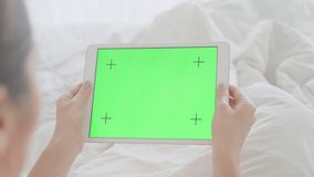 A girl with a beautiful manicure is lying in a snow-white bed and looking at the screen of a tablet with a green screen. A woman on self-isolation holds a tablet with a green screen for cg. - Powered by Shutterstock - Get 15% off with code: PIKWIZARD15