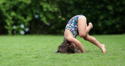Happy child girl rolling on lawn outdoors, tumbling down, kid doing somersault