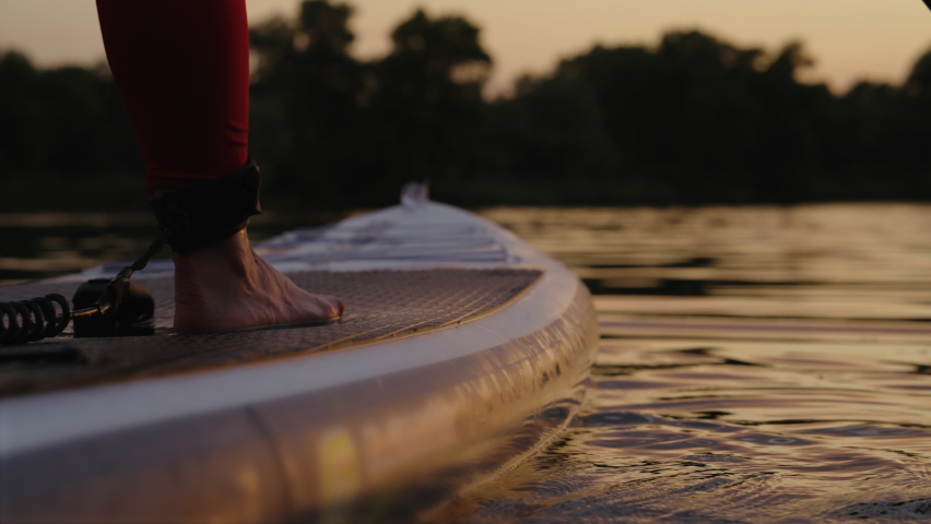 Female feet standing on SUP board while paddling, safety strap attached to ankle. Partial view of woman doing sports on water in the evening. Healthy lifestyle and outdoor activity | Shutterstock HD Video #1078506518