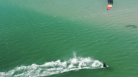 Aerial view of male athlete riding on kiteboard with parachute in Atlantic ocean, Alvor, Portugal, Europe. Overhead view of kitesurfer exercising kiteboarding. Healthy lifestyle concept, 4k footage
