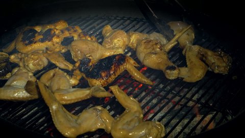 Preparing chicken wings on the grill. Man using metal tongs to turning chicken wings which are being grilled on barbecue. Close-up of the chicken wings. Chicken wings are cooked on the grill. Hot food
