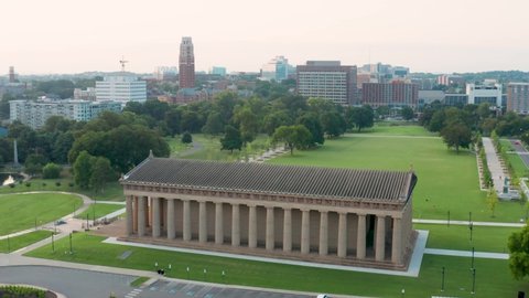 Aerial orbit of Parthenon at Vanderbilt University, Centennial Park. Urban city and skyline in distance.