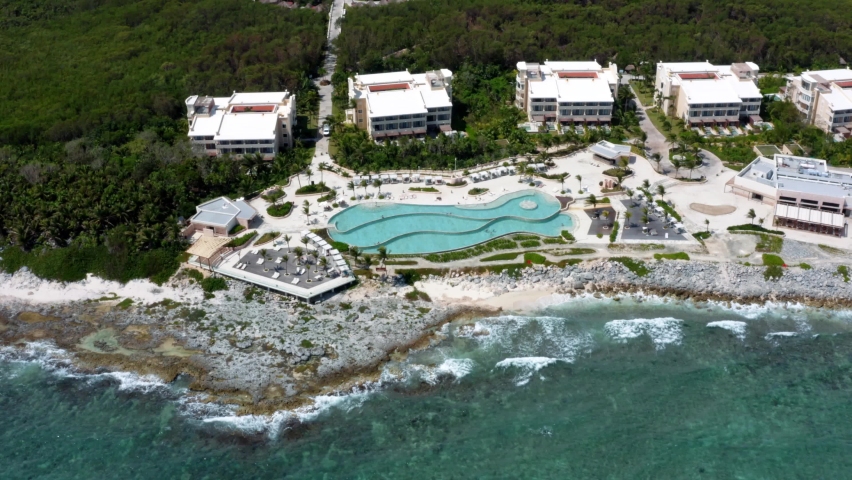 Beautiful spinning aerial drone view of the tropical coastline of playa del carmen with large vacation resorts with pools and bars in Riviera Maya, Mexico on a warm sunny summer day.
